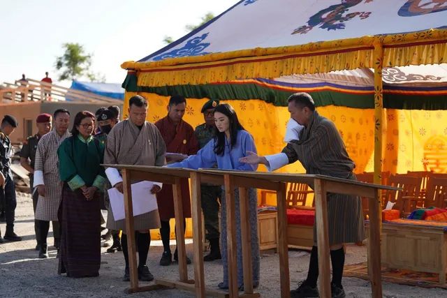 Officials and guests gathered around a wooden table under a decorated tent, looking over plans