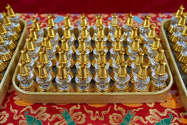 Rows of small gold and glass stupas set out on a tray over red brocade