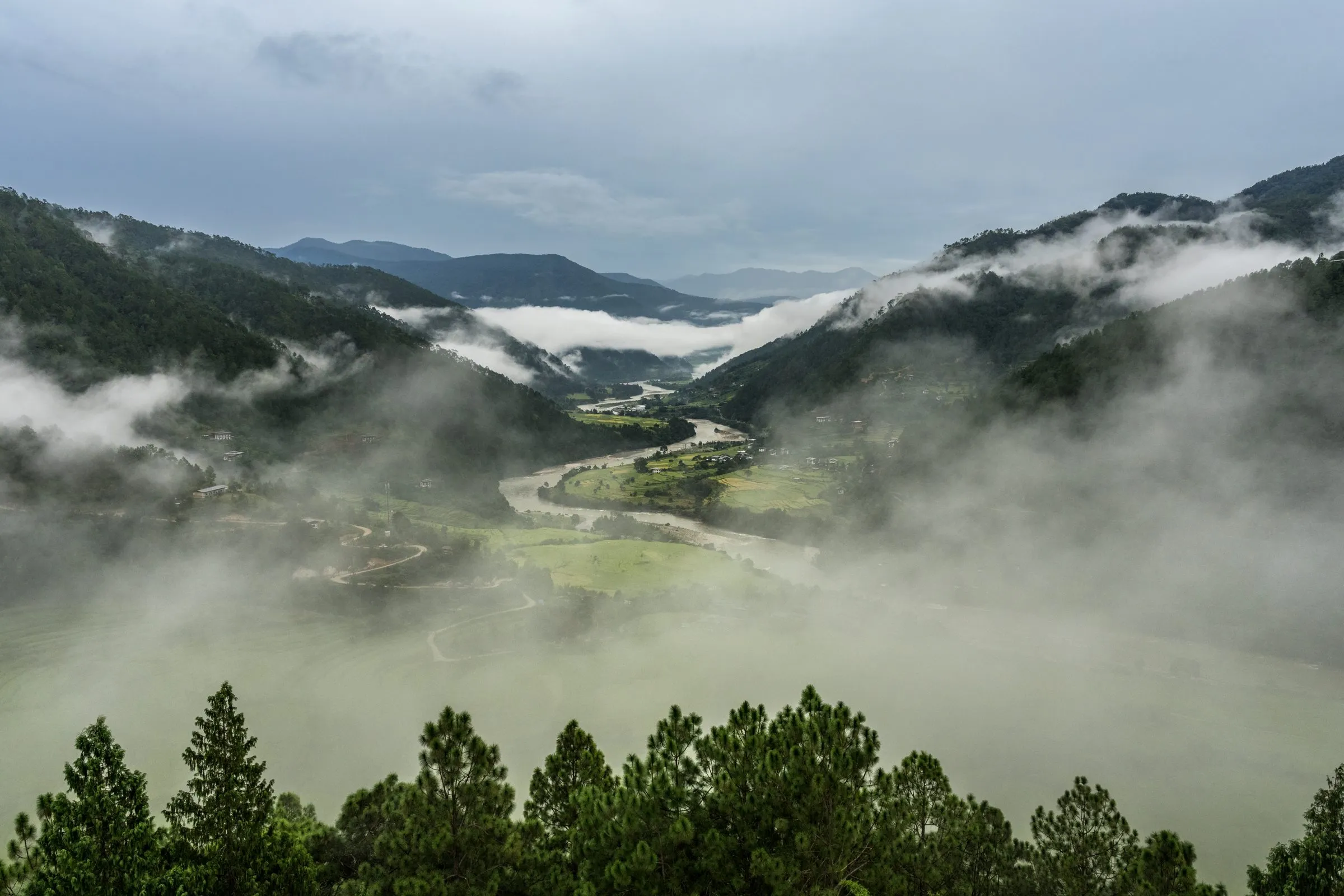 A river valley in Bhutan with mist drifting between forested mountain slopes
