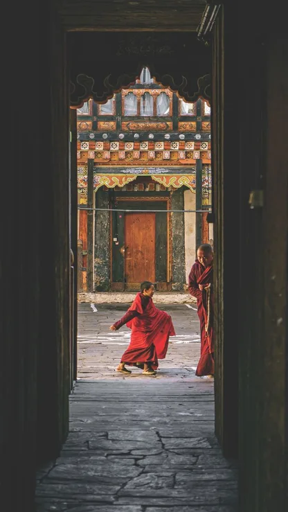 Two young monks in maroon robes in a monastery courtyard doorway, Bhutan