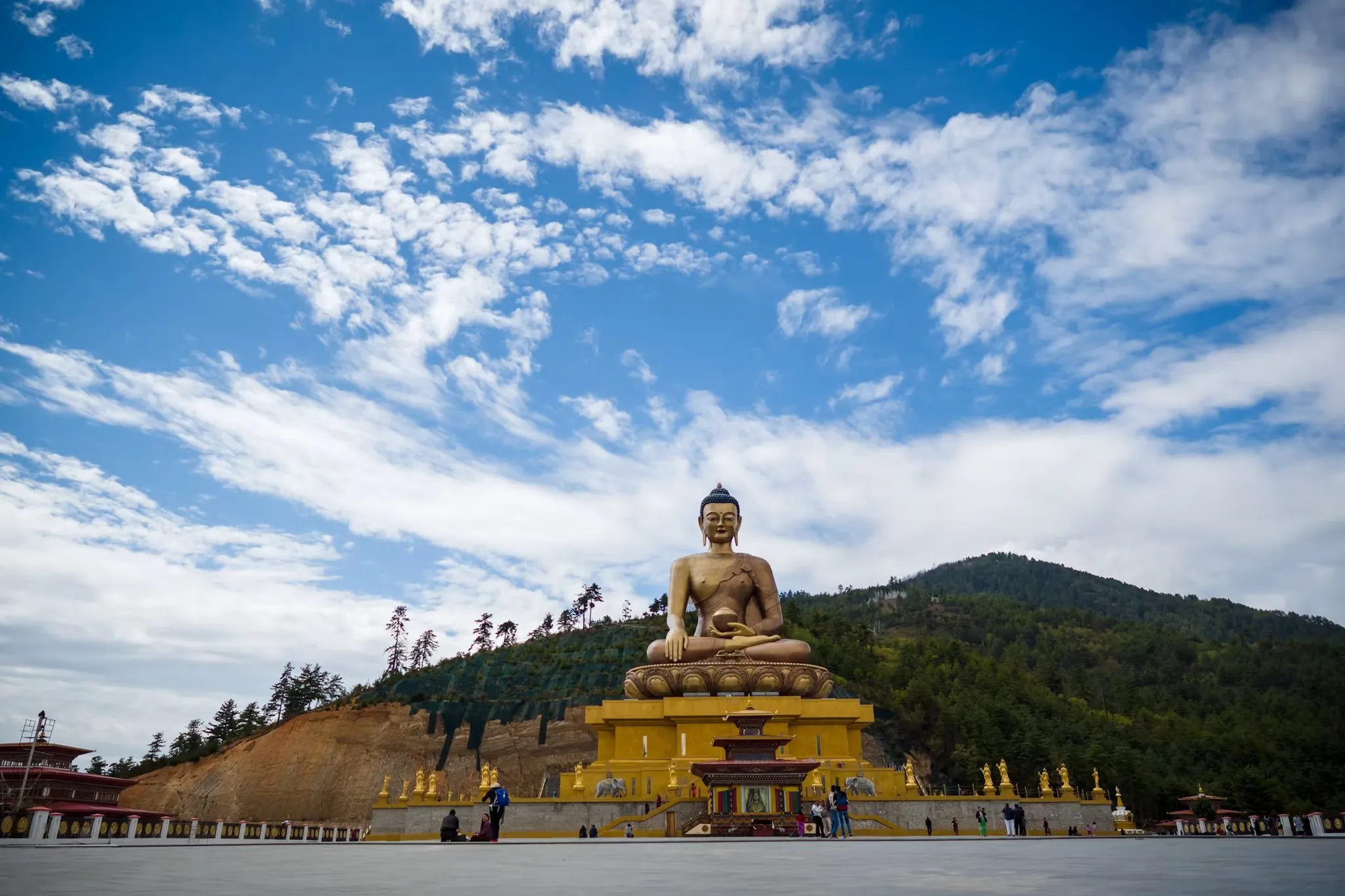 The great Buddha statue at Buddha Point, gold against forested hills under a wide sky of broken cloud