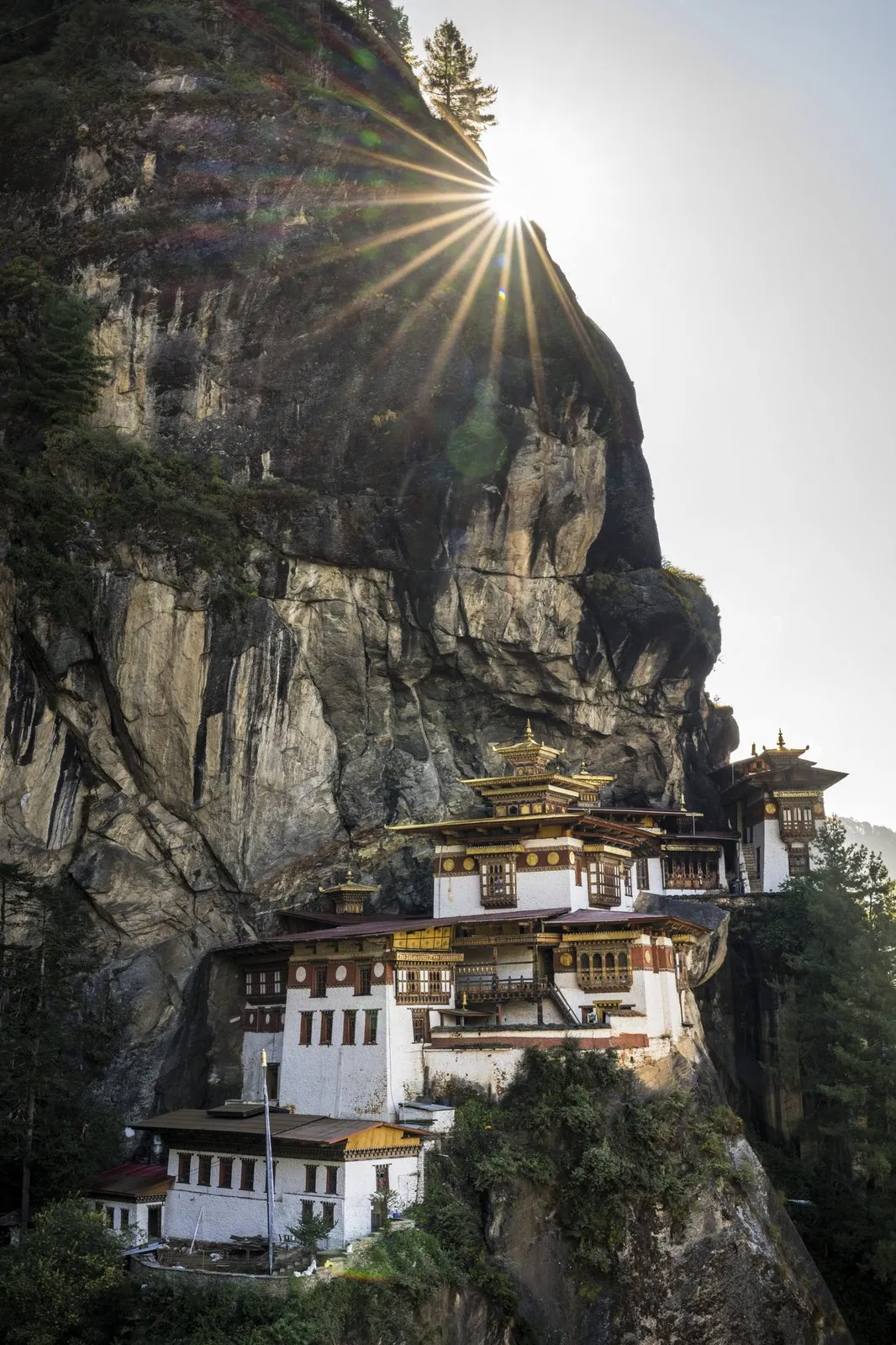 Taktsang monastery clinging to a sheer rock face, with the sun flaring above the cliff