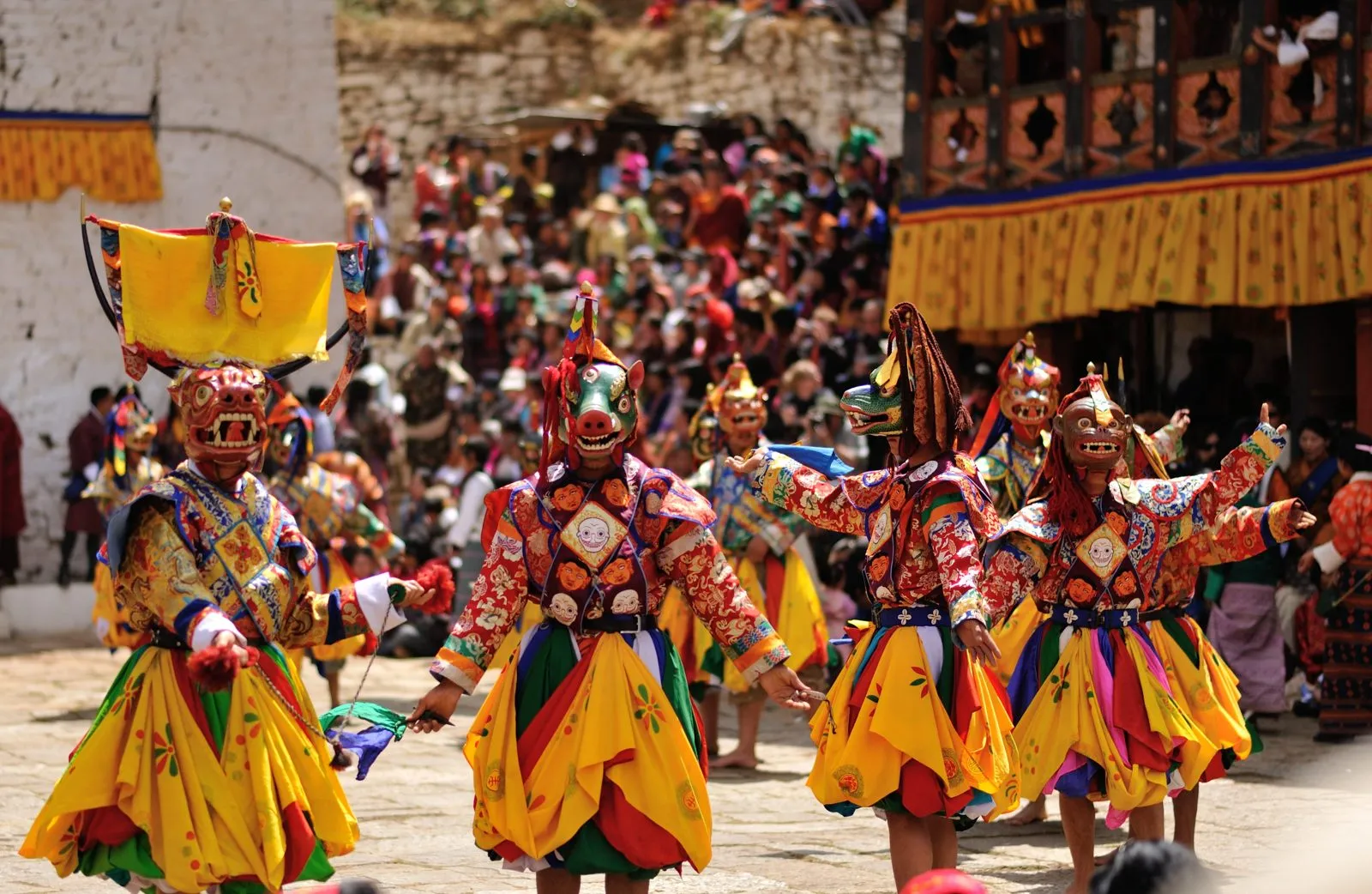 Masked dancers in brocade costumes and animal masks performing in a courtyard before a crowd at the Paro tshechu